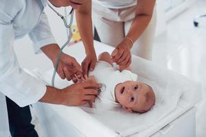 Listening by using stethoscope. Young pediatrician is with little baby in the clinic at daytime photo