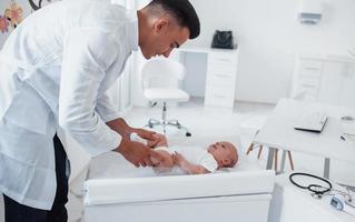 Young pediatrician is with little baby in the clinic at daytime photo