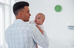 Stands and holds baby on the hands. Young pediatrician is in the clinic at daytime photo