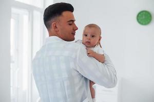 Stands and holds baby on the hands. Young pediatrician is in the clinic at daytime photo