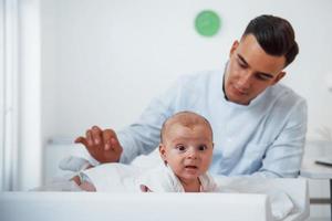 Little baby lying on the table. Young pediatrician is in the clinic at daytime photo