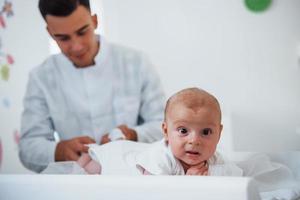 Little baby lying on the table. Young pediatrician is in the clinic at daytime photo