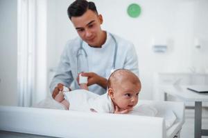 Little baby lying on the table. Young pediatrician is in the clinic at daytime photo