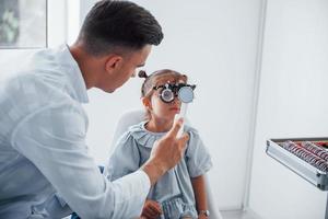 probando la visión. joven oftalmólogo está con una pequeña visitante en la clínica