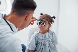 probando la visión. joven oftalmólogo está con una pequeña visitante en la clínica