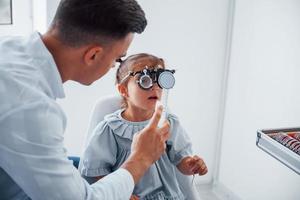 Testing vision. Young ophthalmologist is with little female visitor in the clinic photo