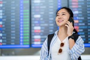 Asian traveler using the smartphone and calling for check-in at the flight information screen in airport, travel and transportation with technology concept. photo