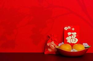 Red envelope packet or ang bao word mean wealth puts with oranges and red bag word is wealth with shadow of peach blossom on red glitter paper background. photo