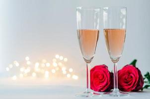 copas de vino rosado espumoso con rosas rojas sobre fondo blanco con luz bokeh para el concepto de aniversario y día de san valentín. foto