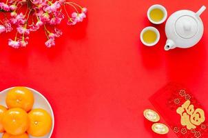 Chinese new year red background with tea set, red envelope packets or ang bao word means wealth, gold ingots, oranges and chinese blossom flowers. photo