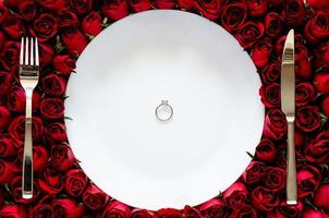 Diamond ring puts on white plate with knife and fork on roses background for dinning to surprise on Valentine day concept. photo