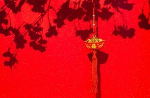 Hanging pendant word mean wealth for Chinese new year ornament with shadow of peach blossom flowers on red glitter paper background. photo
