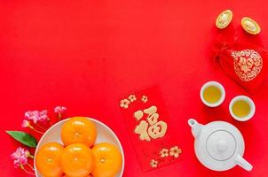 Chinese new year red background with gold ingots, red bag word mean wealth, tea set, red envelope packet or ang bao word means wealth, oranges and chinese blossom flowers. photo