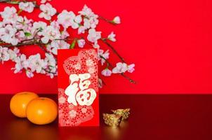Red envelope packet or ang bao word mean wealth puts with oranges and ingots with peach blossom on red glitter paper background. photo