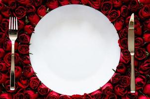 plato blanco con cuchillo y tenedor sobre fondo de rosas para cenar en concepto de aniversario o día de san valentín. foto