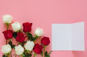 rosas rojas y blancas puestas en un fondo rosa con una tarjeta blanca vacía para el día de san valentín. concepto de fondo plano. foto
