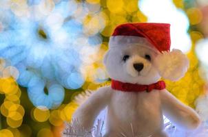 Selective focus on Santa claus teddy bear eyes who wearing hat sitting in front of colorful bokeh lights of Christmas tree. photo