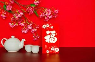 Red envelope packet or ang bao word mean wealth, sentence mean may all go well, great fortune and profit puts with tea set that have chinese blossom on red glitter paper background. photo