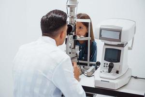 joven oftalmólogo está con una pequeña visitante en la clínica foto