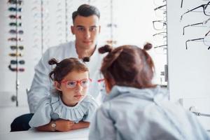 el joven pediatra de bata blanca ayuda a conseguir gafas nuevas para la niña foto