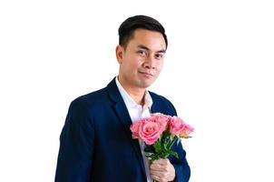 Asian man wearing navy blue suit holding a bouquet of pink roses isolated in white background for anniversary or Valentine day concept. photo