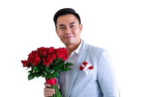 Asian man wearing grey suit holding a bouquet of red roses and red gift box isolated in white background for anniversary or Valentine day concept. photo