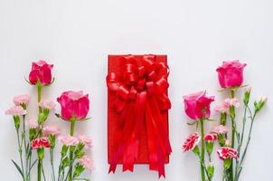 caja de regalo roja con cinta y flores de colores sobre fondo blanco para el concepto de aniversario o día de san valentín. foto