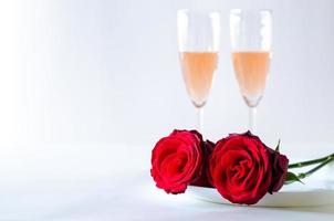 rosas rojas puestas en un plato con copas de vino rosado espumoso sobre fondo blanco para el concepto de aniversario y día de san valentín. foto