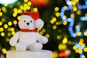 Selective focus on Santa claus teddy bear eyes who wearing hat sitting in front of colorful bokeh lights of Christmas tree. photo