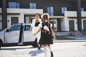 Mother with daughter in school uniform outdoors near white car photo