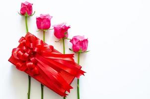 Red gift box with ribbon and pink roses on white background for anniversary or Valentine day concept. photo