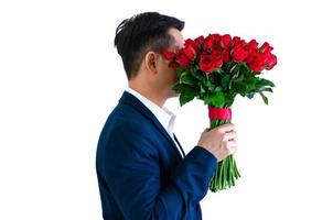 Asian man wearing navy blue suit holding a bouquet of red roses isolated in white background for anniversary or Valentine day concept. photo