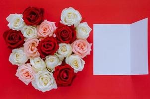 Colorful roses put as heart shape on red background with empty white card for text for Valentine day. Flat lay background concept. photo