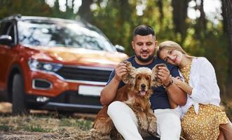 Couple with dog have weekend outdoors in the forest with car behind them photo