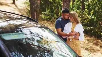 Couple embracing each other in the forest near modern car photo