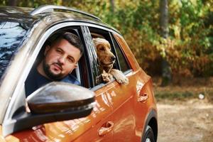 el tipo con su perro se sienta en el camión moderno en el bosque y mira por la ventana foto