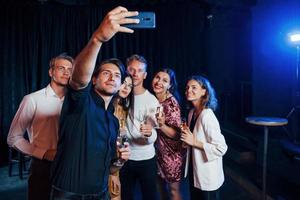 toma autofoto grupo de amigos alegres celebrando el año nuevo en el interior con bebidas en las manos foto