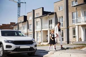 Mother with daughter in school uniform outdoors near white car photo