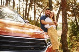 Couple embracing each other in the forest near modern car photo