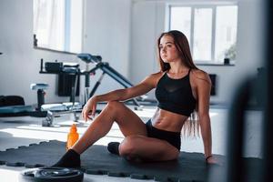 Young fitness woman with slim type of body and in black sportive clothes takes a break photo