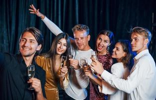 Group of cheerful friends celebrating new year indoors with drinks in hands photo