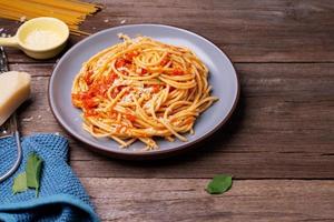 Delicious spaghetti cheese pasta served on a plate Vegetables, Italian tomato sauce and spices arranged on a wooden table, top view photo