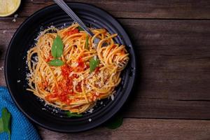 Delicious spaghetti pasta with prawns and cheese served on a black plate on a wooden table Italian recipe tomato sauce vegetables, and spices top view with copy space photo
