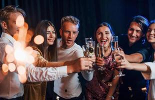 Group of cheerful friends celebrating new year indoors with drinks in hands photo