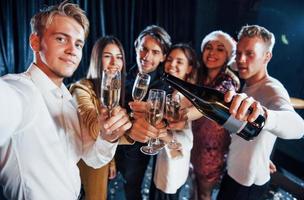 Takes selfie. Group of cheerful friends celebrating new year indoors with drinks in hands photo