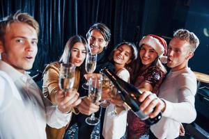 toma autofoto grupo de amigos alegres celebrando el año nuevo en el interior con bebidas en las manos foto