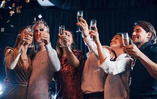 el confeti está en el aire. grupo de amigos alegres celebrando el año nuevo en el interior con bebidas en las manos foto