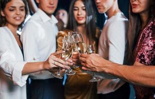 Knocking glasses. Group of cheerful friends celebrating new year indoors with drinks in hands photo