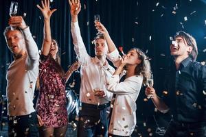 Group of cheerful friends celebrating new year indoors with drinks in hands photo