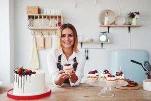 rubia positiva con sus deliciosas galletas y pasteles caseros en la cocina foto